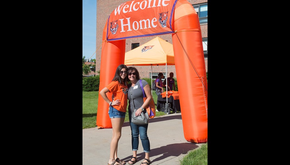 A new student and her parent arriving to Orientation posing underneath an archway